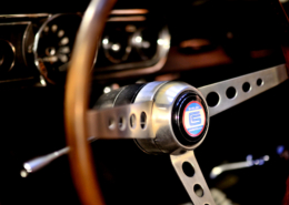 SCP_10 Shelby steering wheel with three spoke brushed chrome center attached to classic wooden steering wheel frame. black blur dash in the background