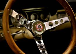 SCP_12 Cobra classic stering wheel with three spoke brushed chrome center attached to classic wooden steering wheel frame. cream blur dash in the background with black inset dials around the instrument panel